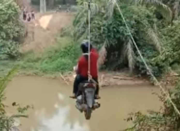 Aksi pengendara motor yang menyeberang sungai di Riau dengan bantuan tali katrol flying fox. (Foto: Instagram @paguyonan/THE EDITOR)