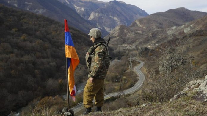 Seorang tentara berdiri di dekat bendera Armenia.