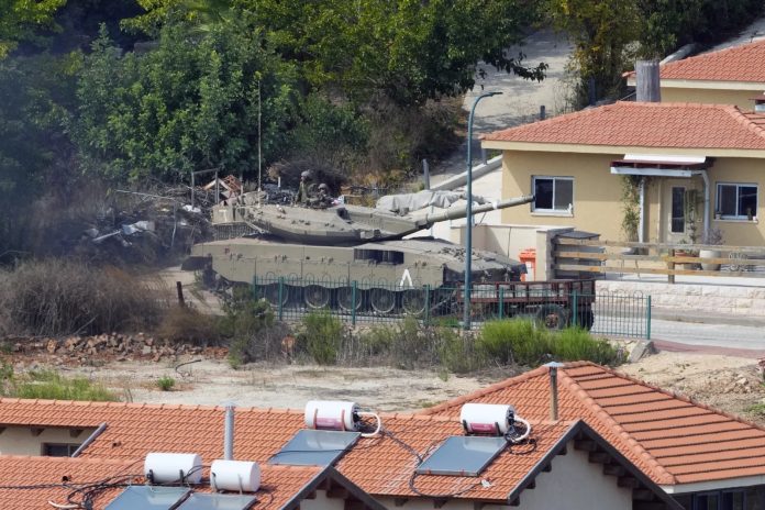 Sebuah tank milik Israel melintas di antara rumah-rumah di kota Metula, Israel, perbatasan Lebanon-Israel di desa selatan Kfar Kila, Lebanon, Senin, 9 Oktober 2023 (Foto: AP/ Hassan Ammar/ THE EDITOR)