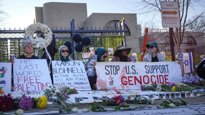 Beberapa orang menghadiri momen penghormatan Aaron Bushnell dengan membawa poster berisi pesan-pesan solidaritas. (Foto: Mark Schiefelbein/AP Photo)