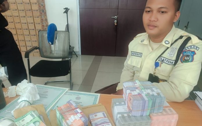 Petugas keamanan Stasiun KA Bandara Medan, Hardiwinata Syahputra, dengan tumpukan uang yang ditemukan di dalam tas yang tertinggal. (Foto: Wahyudi Aulia/MPI)