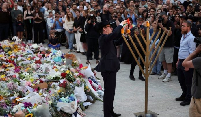 Rabbi Levi Wolff lighting a menorah at Bondi Pavilion beside a memorial for the Hanukkah massacre's victims in Sydney, Australia, earlier today. (Photo: Hollie Adams/Reuters)