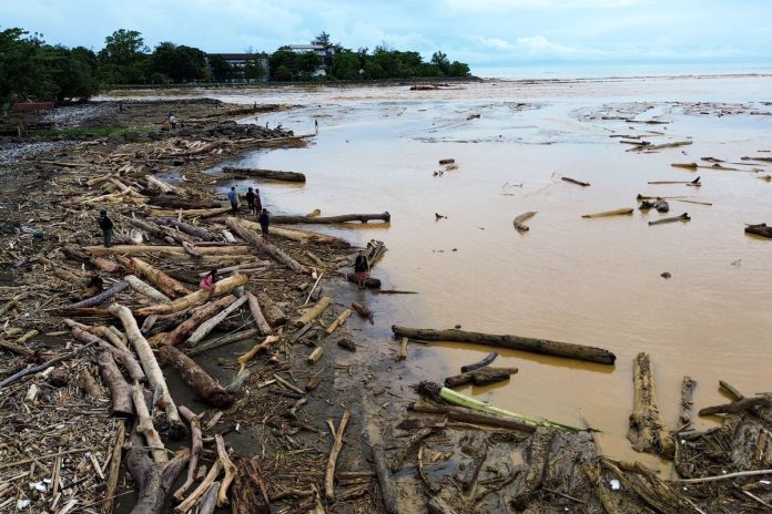 Sejumlah warga berjalan di antara potongan kayu gelondongan yang bertumpuk di pantai Air Tawar, Padang, Sumatera Barat, Jumat (28/11/2025). Sampah kayu gelondongan itu menumpuk di sepanjang pantai Padang pasca banjir bandang beberapa hari terakhir. (Foto: ANTARA FOTO/Iggoy el Fitra/YU/Kompas)
